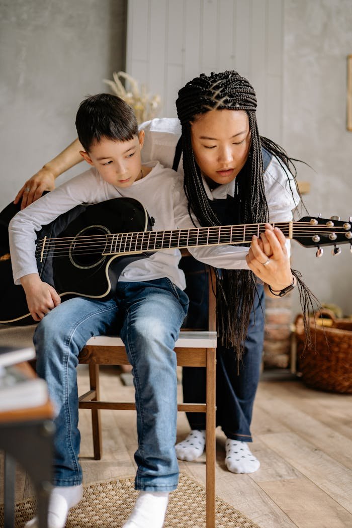 A young boy receiving guitar lessons from a tutor, emphasizing musical learning and instruction.