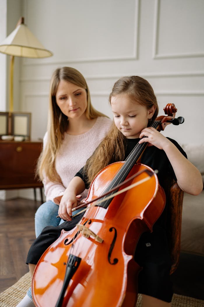Young girl practices cello with attentive teacher in a warm, inviting room.